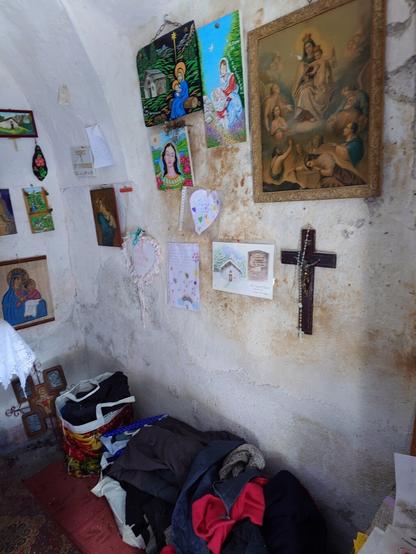 A corner inside the chapel where people put warm clothes and other useful gifts for migrants. On the wall there are many drawings, Catholic paintings and there is a cross with a rosary