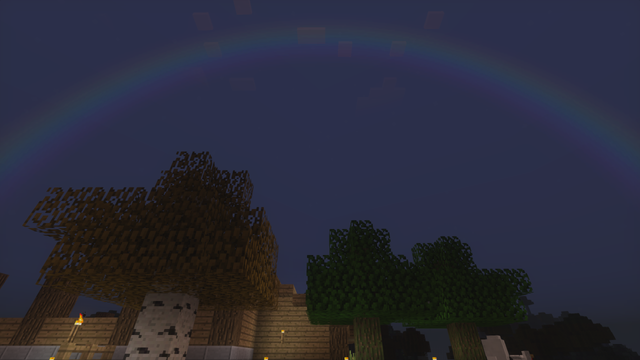 A screenshot from the game Minecraft, looking up at an unfinished cabin behind a few trees.  It is taken in the evening and there's a rainbow stretching across the sky.