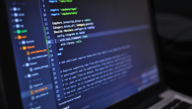 A dark room with a monitor showing a dark blue background with colorful lines of source code.