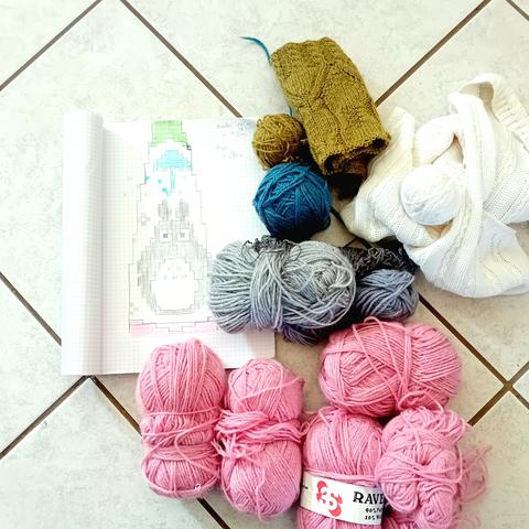 À gauche, il y a un dessin pour tricot sur une feuille quadrillé de cahier. Il y a un parapluie bleu et totoro en dessous sur fond blanc, en dessin pixel. À droite du dessin, il y'a plusieurs pelotes de laine, vert, blanc, bleu, gris, rose.