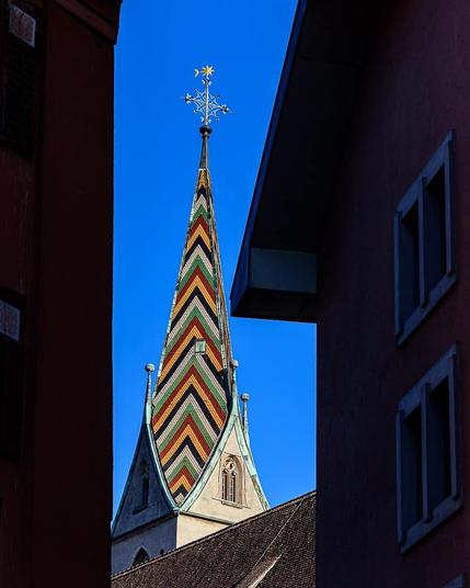 A medieval Bell tower against blue sky, framed by the black silhouettes of surrounding buildings