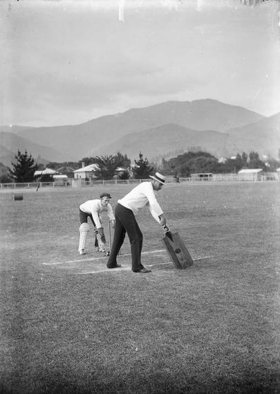 Black-and-white photo: Comic photograph of a cricket match, Nelson. ca. 1910s. Photographer, Frederick Nelson Jones. Description: Comic photograph of an unidentified wicket keeper and batsman playing a game of cricket with an oversized cricket bat. Citation: Jones, Frederick Nelson, 1881-1962: Negatives of the Nelson district. Ref: 1/2-028985-G. Alexander Turnbull Library, Wellington, New Zealand. https://natlib.govt.nz/records/22635935