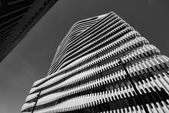 View along the facade of a high-rise building into the sky. The design of the façade is reminiscent of zippers.