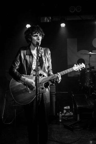 Black and white portrait orientation shot of a singer on stage singing and playing an acoustic guitar
