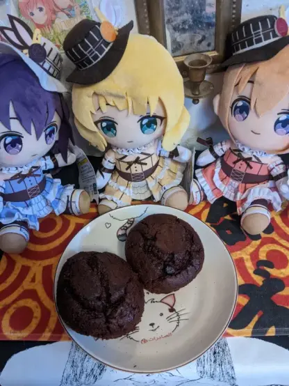Two chocolate muffins on a neko plate. Fancy Rize, Syaro, and Cocoa plushies are looking at them.