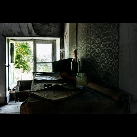 Photography in color of an old room, with a desk. On this desk, old papers and and old bottle . Urban exploration, exploration of an abandoned castle