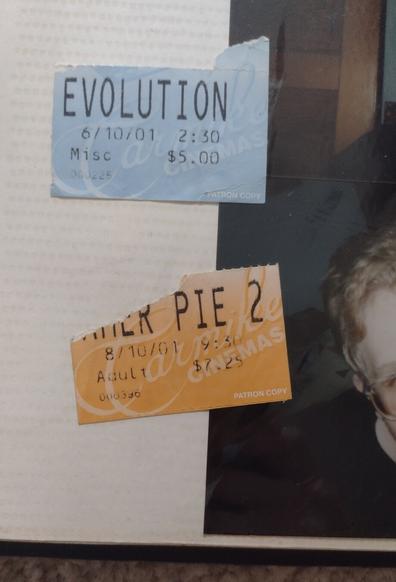 A photo album page with two movie ticket stubs, "Evolution" dated 6/10/01 and "Amer Pie 2" dated 8/10/01, along with a fragment of a photograph showing part of a young white man's face and glasses.