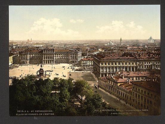 The image shows a panoramic view of St. Petersburg's cityscape from an elevated vantage point, capturing the vast expanse of architectural structures and open spaces. Prominently featured in the foreground is Palace Square with its iconic equestrian statue, which appears to be that of Emperor Nicholas I, surrounded by classical buildings displaying detailed facades. The square opens up into a wide avenue leading toward the center of the image where several notable domed churches are visible against the skyline.

The coloration and photographic style suggest it was taken during or shortly after the late 19th century, with sepia tones prevalent in older photographs from that period enhancing historical ambiance. Buildings exhibit ornate decorations typical of Russian architecture around this era. The sky is partly cloudy but allows for a clear view of distant buildings on the horizon, possibly indicating St. Petersburg's expansive urban sprawl.

The image carries an inscription at its base which reads "810.P.Z.-St. Petersbourg," translating to "Place du Conseil de l'Empire" and dating it between approximately 1890-1900. The photograph is a product of Léon Loener's photochrom company, known for creating vividly colored images from photographic negatives during that time.

In summary, the image captures an early snapshot of St. Petersburg’s urban landscape as viewed by one looking westward towards Palace Square and beyond to [...]