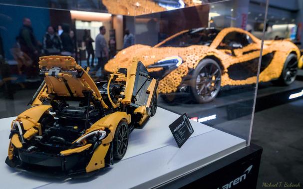 McLaren P1 made of Lego bricks, model sized, in the foreground of another P1 made of Lego bricks, life sized, slightly out of focus.