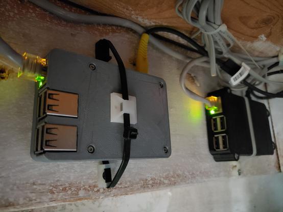 Two Raspberry Pi 3s in 3D Printed Cases. They are both screwed and Zip-tied to the wall at a house's basement. they have only a power cable and an Ethernet cable connected to them. the ethernet lights are active.