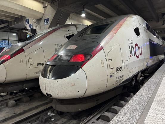 Vue de la rame TGV 850 en livrée Carmillon. 
A quai voie 4 en gare de Paris Montparnasse.
Les feux rouges sont allumés.
Derrière on aperçoit la rame 269 Duplex première génération rénovée Océane-Like en livrée Carmillon elle aussi.