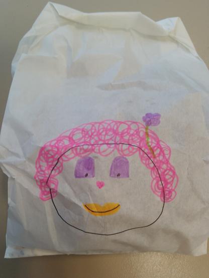 Auf einer Brötchentüte hat die Mutter einer Schülerin ein fröhliches Gesicht in bunten Farben gemalt.