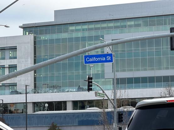 A sign for California St, typeset in white Helvetica on a blue background, hanging from a traffic light post.
