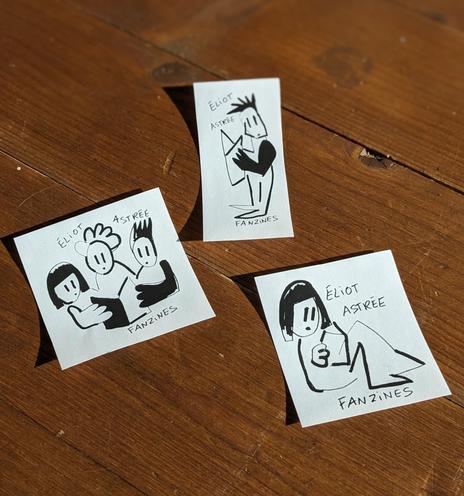 3 stickers en noir et blanc posé sur un plancher. Ils représentent des personnes en train de lire des fanzines dans un style naïf. Sur chaque sticker il y a écrit "Éliot Astrée Fanzine"