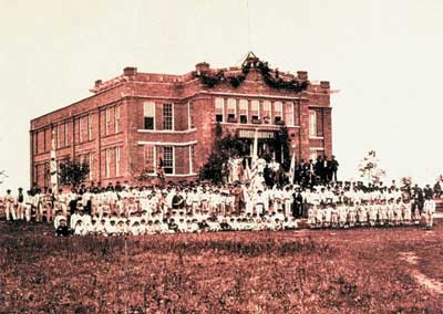 Historisches Farbfoto eines Turnfestes in New Ulm, USA. Zu sehen ist ein Gebäude, vor dem sich eine große Menge Turner in Sportkleidung versammelt hat.