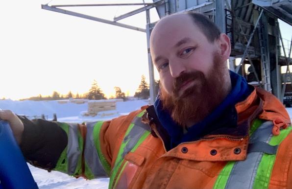 A vid white male with a large white beard offers out a hug. The sun shine brightly behind him
