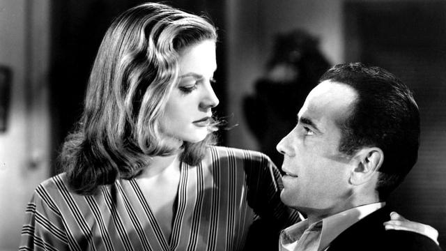 A shot from the 1944 film "To Have and Have Not" starting Lauren Bacall and Humphrey Bogart.

This is a black and white photograph. We can see the top portions of two people, a middle aged man and a younger woman. She is wearing a striped dress or blouse, open at the neck, while he has on a white shirt and dark suit jacket, but no tie.

They are sitting very close to each other and looking into each other's eyes. There is definite chemistry between them.