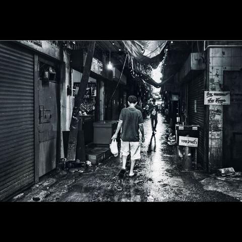 A B&W photography of a street in China Town, wet and dirty  place. 2 people are walking