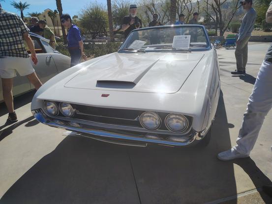 The front of this near-custom Ghia roadster has quad headlamps and a low, flat hood scoop.  The car is a creamy white with chrome bumpers, low-slung and wide.