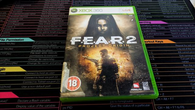Zdjęcie przedstawia pudełko z grą „F.E.A.R. 2: Project Origin” na konsolę Xbox 360. Na okładce widnieje mroczna grafika – w tle znajduje się postać dziewczynki o długich, ciemnych włosach, a na pierwszym planie uzbrojony żołnierz w futurystycznym pancerzu, otoczony iskrami i zniszczeniami. Na dole okładki widoczna jest klasyfikacja wiekowa „18+” oraz logotypy Monolith Productions i Warner Bros. Games. Pudełko ma charakterystyczny zielony kolor, typowy dla gier na Xbox 360. W tle zdjęcia znajduje się kolorowa ściągawka z komendami systemu Linux.