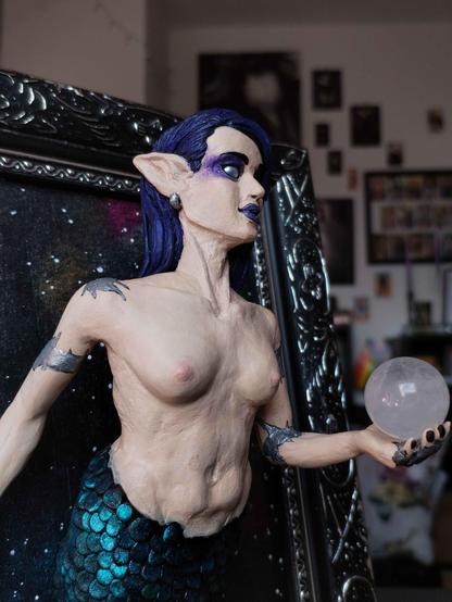 the same mermaid, now in soft lighting and from the side, a closer look at the details. She has pointy ears, wearing silver earrings. Her scales are individually sculpted and all reflect the light a bit differently.