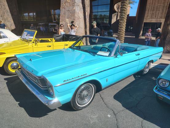 A 1965 Ford Galaxie 500 convertible is pictured with the top down, seen from the front.  The car is light aqua blue with a slightly darker aqua bench seat interior.  I have always loved styling with a bold, straight beltline; this model year of Ford defines the concept.  I mentioned our family's 1965 Ford Custom sedan I learned to drive on -- my Dad was a professor, and that year he was in sabbatical residence at the geology school at the University of Kansas in Lawrence.  Needing a car there, Dad went to our Ford dealer, a family friend from church, and said "give me the cheapest thing on your lot."  The Custom was the entry level big Ford.  It was white with a tan bare-bones interior, had an AM radio and a heater, and nothing else.  It was a 2-barrel 289 V8 with automatic, no power steering or brakes, no air conditioner.  When I drove it, people frequently slowed down around me, thinking it was an unmarked police car.