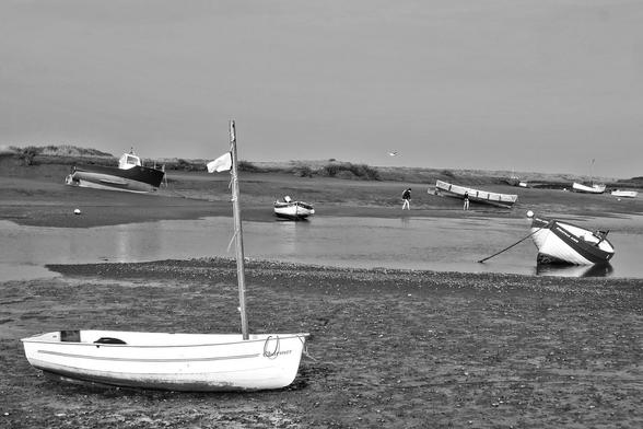 Overy harbour at dead low water, two young explorers about to paddle back across the creek from the marsh, scattered boats including a dinghy with a home-made looking mast and plain burgee, black and white