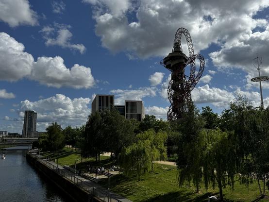 A beautiful sunny spring day. There’s a small river to the left. A path goes along the riverbank. In the background is a helter skelter attraction, the Orbit in Queen Elizabeth Olympic Park, Stratford, East London