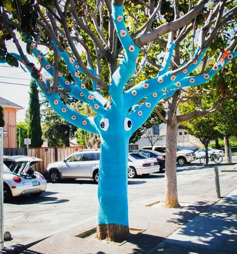 You are greeted by tree transformed into a blue squid with the trunk and branches covered in blue knit fabric. Crocheted eyes look out from the trunk while the branches are covered with crocheted orange suckers. A shrimp sits lazily on one of the branches.