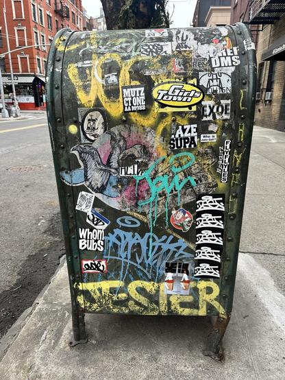a mailbox covered with graffiti and stickers over an old wheatpaste on a street in manhattan
