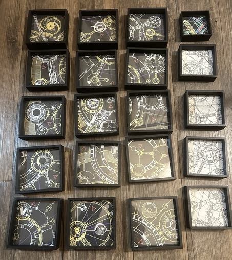 About 20 small geometric abstract art pieces in gold and silver acrylic on black paper, strongly resembling gears and clockwork