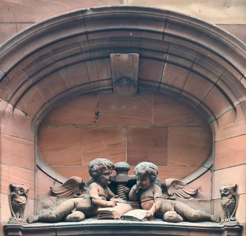 A sculpture of two putti with a printing press with an owl looking on from either end.
