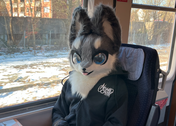 Avalanche sitzt auf einem Einzelsitz in einem InterCity alter Baureihe und lächelt in die Kamera. Das Bild zeigt sie im Partial mit einem schwarzen Hoodie.