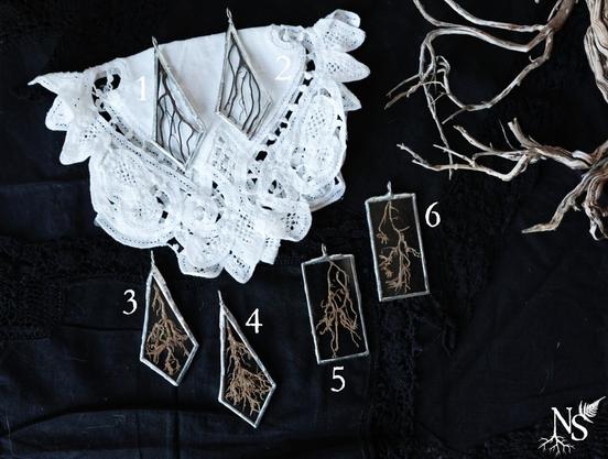 English 6 stained glass pendants showcasing roots bits laying on black and white crochet doilies. Some pendants are rectangles, some are like angular drops.
❉
Français 6 pendentifs en vitrail mettant en valeur des morceaux de racines posés sur des napperons au crochet noir et blanc. Certains pendentifs sont des rectangles, d’autres ressemblent à des gouttes angulaires.