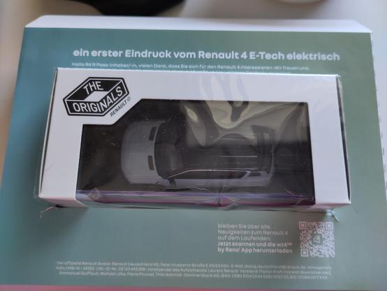 Nach dem Auspacken ist ein klenerer Karton zu sehen. Er ist weiß und hat eine große Folie als Sichtfenster. Im Karton ist ein Modellauto zu sehen.
Der weiße Karton steckt in einer grünen Pappumrandung. In weißer Schrift steht oben : " ein erster Eindruck vom Renault 4 E-Tech elektrisch "
Unten links ist ein QR Code zu sehen.