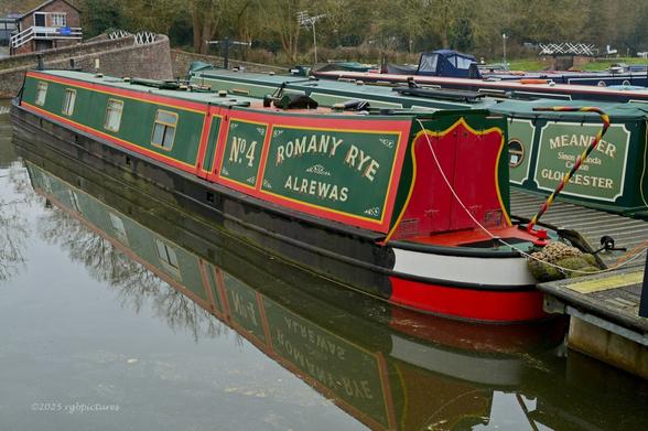 A moored canal boat with it's reflection in cold, grey water.