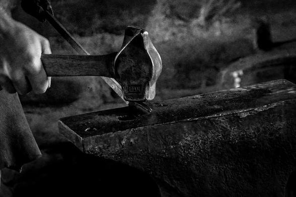 A blacksmith swings a hammer against a hot piece of metal on an anvil at Fort William, a former fur trading post in Thunder Bay, Ontario.