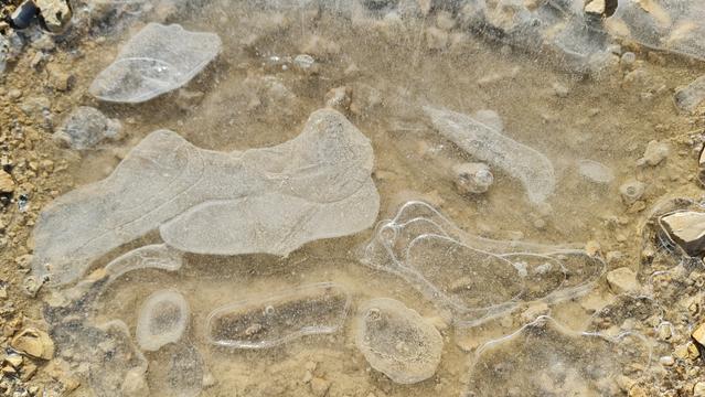 Gefrorene Pfützen im Schotterweg, einmal gesamtsicht, einmal von nahe die Luftblasen im Eis