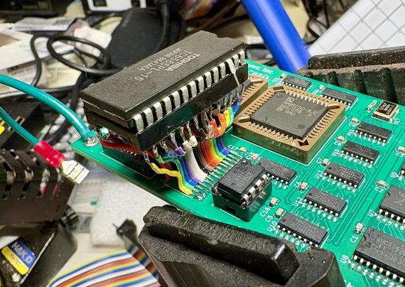 A DIP chip in a socket, which has been connected to footprint on a PCB meant for a much smaller chip using a pair of ribbon cables. This makes the socket float above the board.