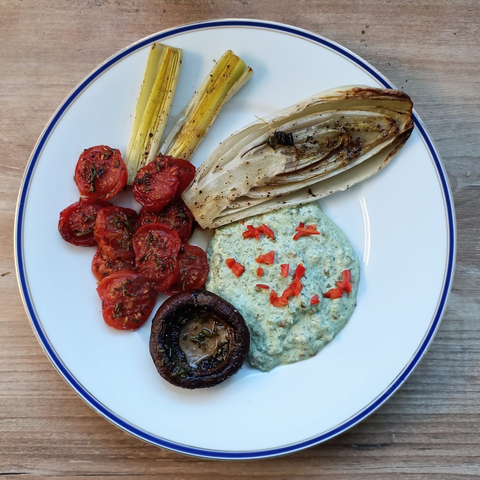 Das fertige Gericht auf dem Teller - halbierte Tomaten, halbierter Chicorée, halbierter Lauch, ein großer Champignon und ein großer Klecks grünliche Creme mit fein geschnittener Chili