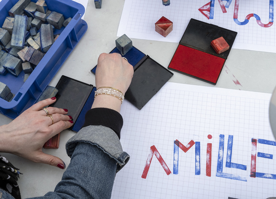 Outdoor workshop, people handling red and blue stamps to write words. Photo: Anabelle Michon