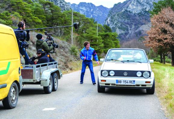 Photo d’une équipe de tournage dans une remorque attachée à un véhicule utilitaire jaune, lors de la capture d’une scène où Côme se tient debout sur une route de campagne et s’approche d’une Golf blanche.