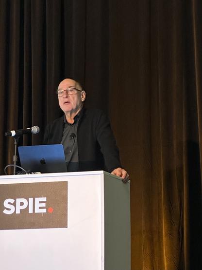 Man speaks from lectern marked with logo of SPIE