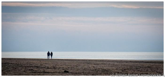 A lonely couple stands at the seafront and looks at an endless horizon.