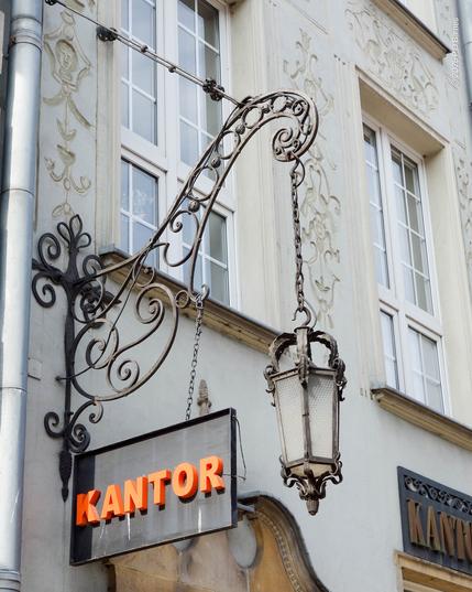 An elegant French-curve wrought-iron bracket and lantern, also holding a currency-exchange sign/