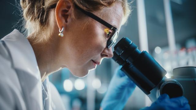 Random corporate image of a white woman looking through a microscope