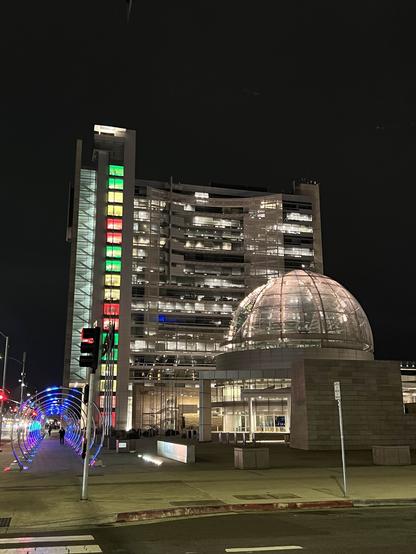 San José City Hall tower and rotunda dazzling at night with all the lights on. In the foreground is a series of illuminated arches over the sidewalk.
