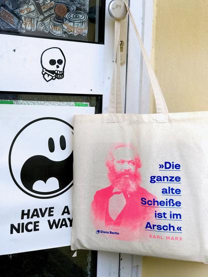 »Die ganze alte Scheiße ist im Arsch«, schrieb Karl Marx an Friedrich Engels zur Wirtschaftskrise 1857, nachzulesen in den Marx-Engels-Werken Band 29, Seite 239. Gedruckt auf unserer Marx Tote Bag, die im Foto an der Tür zum Nachladen in Hamburg hängt.
