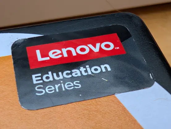 Model sticker saying "LENOVO (tm) Education Series" stuck neatly in the corner of a laptop lid on top of some other decorative stickers.