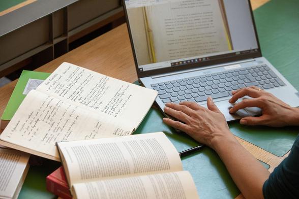 Eine Person arbeitet in der Bibliothek des DHIP mit Notizen, verschiedene Bücher sowie ein Laptop.